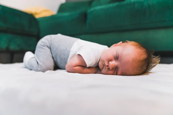 在绿色沙发旁边的地板上躺着穿着婴儿衣服 留着浅色短发的白人男婴 他的头对着镜头 新生儿 横向室内拍摄 高质量的照片 — 图库照片