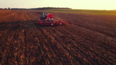 Ekme makinesi olan traktör kahverengi tarladan geçiyor. Yan tarafında yeşillik ve soluk arkaplan var. Sabah manzarası. Yatay çekim. Yüksek kalite 4k görüntü
