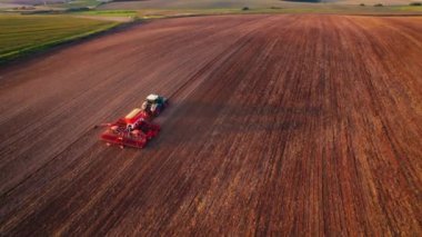 Sarı güneş kahverengi tarlada parlıyor. Yeşil traktörlü, ekme makineli, döküm gölgesinden geçiyor. Çiftçilik ve tarım. Yatay çekim. Yüksek kalite 4k görüntü