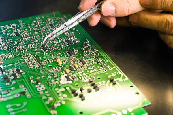 Repairing process of a broken PCB. Professional caucasian engineer manually removing broken electric components and replacing them with new ones with tweezer. Closeup shot. High quality photo