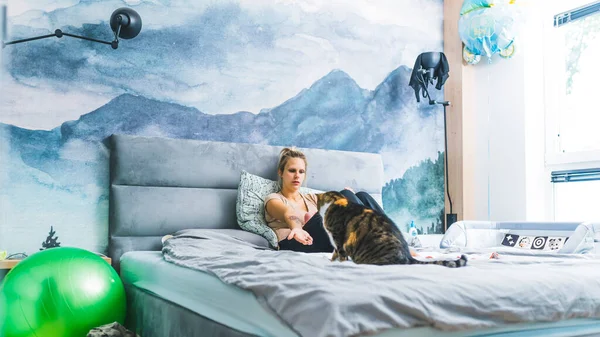 금발의 여자가 무릎을 아기와 침대에 있다가 동물인 고양이에게 내밀었다 고품질 — 스톡 사진