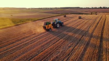 Golden field with bales of hay and blue tracktor stacking hay with green fields in the background. Agriculture. Horizontal shot. High quality 4k footage