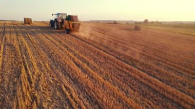 Gün batımında traktör saman silindiri makinesiyle tarladan geçiyor. Yüksek kalite 4k görüntü