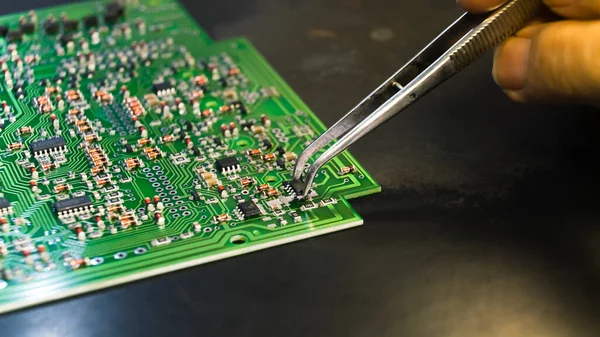 Surface-mount technology concept. Closeup shot of metal tweezers used by hand of an unrecognizable caucasian professional repairman placing small electric components onto PCB. High quality photo