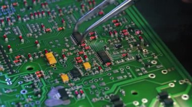 PCB, elektrik bileşenleriyle basılmış devre kartı ve lambayla daha fazla parça yakan cımbızla tutturulmuş bir el. Elektronikleri monte ediyorum. Tamirci. Yüksek kalite 4k görüntü