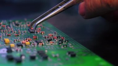 PCB baskılı devre kartının yakın çekim görüntüsü, monte edilmiş elektrik bileşenleri ve parçaları değiştiren cımbızla el. Elektronik tamir. Hassasiyet ve odaklanma. Yatay çekim. Yüksek kalite 4k