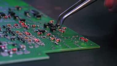 PCB baskılı devre kartına cımbızla elektriksel bileşenler monte eden tanınamaz haldeki birinin yakın çekim görüntüsü. Elektronik tamir. Kusursuz bir iş. Yatay çekim. Yüksek kalite 4k