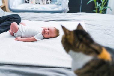 Yatağa uzanmış, yanında oturan kediye bakan yeni doğmuş tatlı bir çocuk. Yüksek kalite fotoğraf