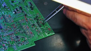 El sıkışan cımbızlar, baskılı devre kartı PCB 'nin detaylı yüzeyinde elektrik parçaları birleştiriyor. Onarım teknolojisi. - Aynen öyle. Yakın plan. Yüksek kalite 4k görüntü