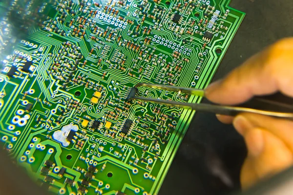 The man hand of the technician assembling manualy electronic components and microcircuits on printing circuit board with printed multi wire connections. Electronics Manufacturing Services. High