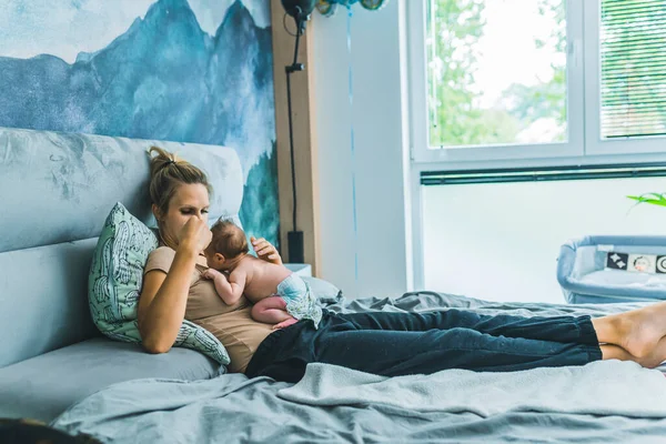 Beyaz tenli güzel genç anne yatakta dinleniyor ve yeni doğmuş oğlu bebek beziyle karnının üstünde, tasarlanmış mavi renklerde bir bebek odasında yatıyor. Yüksek kalite fotoğraf