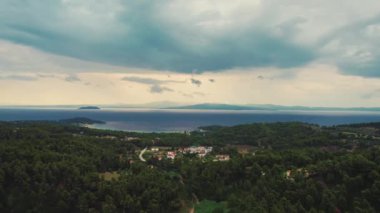 Halkidiki 'nin Yunanistan' daki hava manzarası. Yunan tarzı evleri ve tatil köylerini çevreleyen yoğun ormanlar. Güzel bir sahil ve arka planda başka bir ada. Bulutlu gökyüzü. Yüksek kalite 4k görüntü