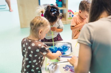 Çocuklar küçük tüplere üfleyerek anaokulunda suluboya boyayla resim yapıyorlar, orta boy anaokulu konsepti. Yüksek kalite fotoğraf