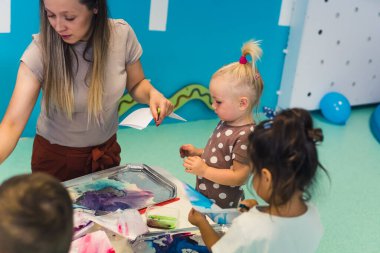 Öğretmen anaokulunda sevgili çocuklarıyla resim yapma tekniklerini kullanıyor. Yüksek kalite fotoğraf