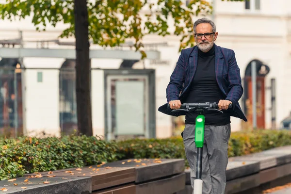 Commuting to work using electric scooter. Older generation embracing modern trends. Outdoor medium shot of elderly good-looking beaded man riding on e-scooter to work. High quality photo