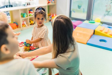 Anaokulu öğrencileri ve anaokulunda kinetik kumla oynayan bir öğretmen, arka planda oyuncaklar ve oyun alanı. Yüksek kalite fotoğraf