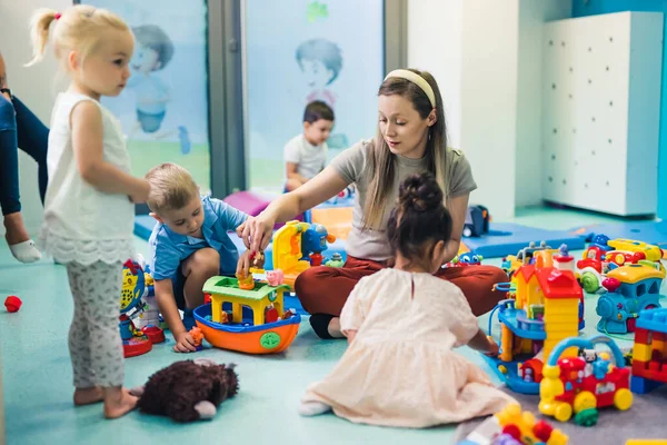 our teacher is the best - lovely kids playing with their young teacher, kindergarten playground . High quality photo