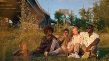 Dışarıda boş vakit geçirmek için. 30 'lu yaşlarda, şenlik ateşinin yanında çimlerde oturan ve konuşan çok kültürlü ve çok ırklı bir arkadaş grubu. - Evet. Yüksek kalite 4k görüntü