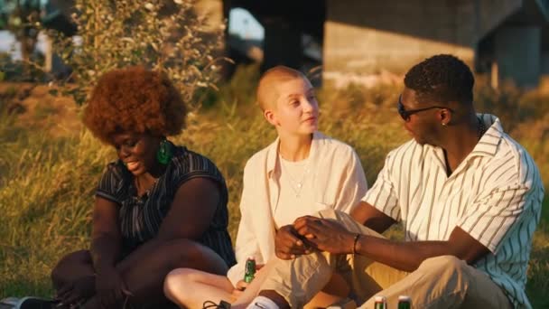 美丽的黑人妇女 戴着生动的绿色耳环 蓬松的红色非洲发式坐在她的朋友旁边 听着他们的谈话 户外枪击案Meadow野餐高质量的4K镜头 — 图库视频影像