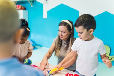 Koyu saçlı beyaz bir çocuk ve güzel bir öğretmenin kinetik kumla eğlenirken orta boy fotoğrafı, anaokulu konsepti. Yüksek kalite fotoğraf