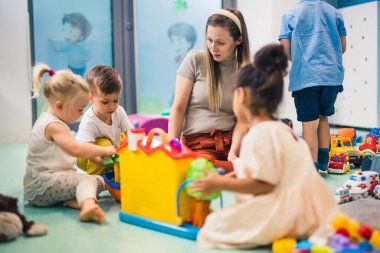 Bir şehir inşa etmek istiyoruz, öğretmenim beyaz sevimli çocuklar güzel öğretmenleriyle, anaokuluyla, arka planda oyuncaklarla dolu bir odada eğleniyorlar. Yüksek kalite fotoğraf