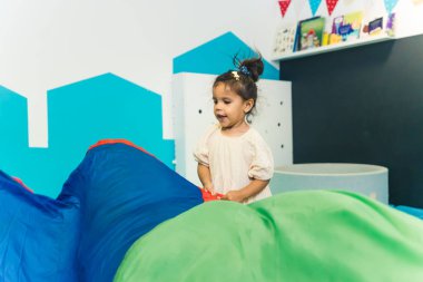 Anaokulunda renkli kumaşlarla oynayan sevimli bir kızın orta boy fotoğrafı. Yaratıcılık oyunu konsepti. Yüksek kalite fotoğraf