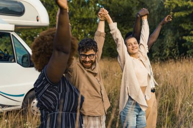 Arkadaşlıkta kahkahanın gücü. Elleri havada yan yana duran farklı ten renginde beş kişi. Arka planda beyaz karavan var. Çayır. Yüksek kalite fotoğraf