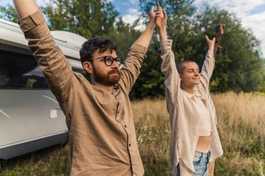 Minibüste seyahat ederek özgürlük duygusuna ulaştım. Açık havada, elleri havada üç kişinin yakın plan çekimleri. Gözlüklü ve bej gömlekli beyaz sakallı adama odaklan. - Evet. Yüksek