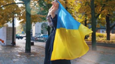 Ukraynalı destekçi gururla arkasında mavi-sarı bayrak tutuyor, etrafında dönüyor ve yüzünde bir gülümsemeyle kameraya bakıyor. 50 'li yaşlarda beyaz bir işadamı. Yüksek kalite 4k görüntü