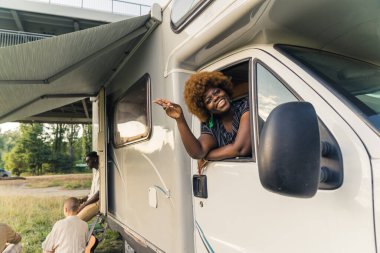 Seyahatlere açık ol. Minibüsle seyahat etmek için modern fikirler. Afro saçlı, olumlu gülümseyen siyah kadın yolcu penceresinden eğiliyor ve kameraya el sallıyor. - Evet. Yüksek kalite