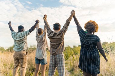 Çayırın ortasında el ele tutuşan dört kişilik çok uluslu bir grup. Yaz seyahati. Arkadan bak. Yüksek kalite fotoğraf