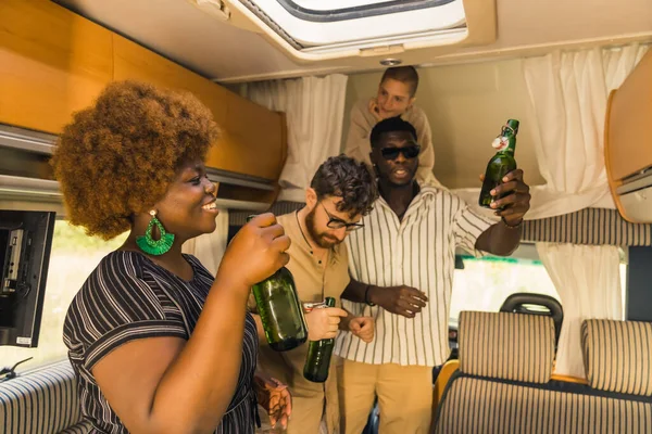 Interracial group of friend-travelers dancing in van living room, holding green glass bottles full of tasty beer, and laughing. Millennials at a party. High quality photo