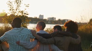 Bir grup yetişkin arkadaş nehir kenarında kamp yapıyor. Birbirlerini kucaklıyor, rahatça sallanıyorlar. Çeşitli arkadaş grupları. Yatay açık hava çekimi. Yüksek kalite 4k görüntü