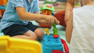 Kreşteki bir grup küçük çocuk renkli eğitim oyuncaklarıyla oynuyorlar. Öğretmenle yaratıcı oyun zamanı. Kapalı alanda yatay çekim. Yüksek kalite 4k görüntü