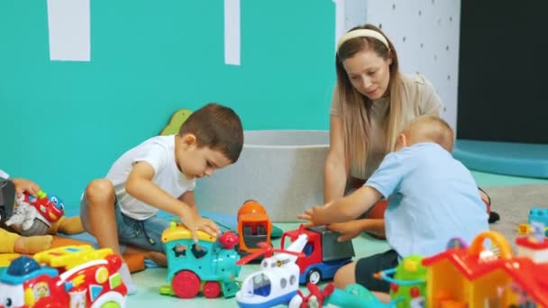 Zwei Kleine Jungen Spielen Mit Spielzeugfahrzeugen Und Ihre Lehrerin Beobachtet — Stockvideo