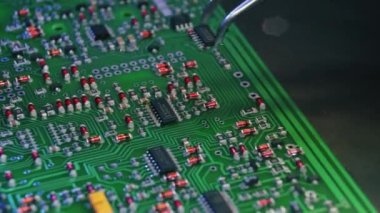 İnsan ve modern teknoloji kavramı. Robotlar işçilere karşı. Yazılı devre kartına elektrikli parçaları yapıştıran gümüş cımbız aletinin yakın çekimi. Yüksek kalite 4k görüntü