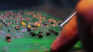 Tanımlanamayan Kafkas mühendisleri elektrik bileşenlerini yeşil PCB 'ye elle monte ederken el ele tutuşuyorlar. Cımbız benzeri aletin yakın plan çekimi ve elektrikli parçaları baskılı devre kartına yapıştırmak. Yüksek