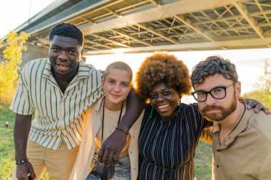Kameraya bakıp gülümseyen dört kişilik çok kültürlü bir grubun açık hava portresi. Birliktelik ve dostluk. Yüksek kalite fotoğraf