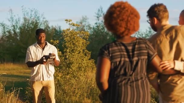 户外黄金时间 夏天的时候身穿条纹白色衬衫的中年黑人男子用模拟相机对着他的多种族朋友拍照 高质量的4K镜头 — 图库视频影像