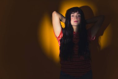 Güzellik endüstrisi reklamı. Çekici, uzun saçlı, sıradan giyinmiş beyaz kadın model kolları havada daire şeklinde duran, doğrudan kameraya bakan sarı projektör. Yüksek kalite fotoğraf