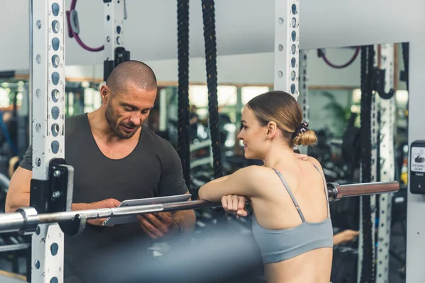 Young attractive skinny caucasian girl in her 20s listening to her private personal instructor giving her feedback after strength test. Medium closeup shot, gym interior. High quality photo