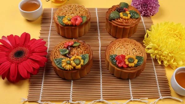 Colorful flower decorated moon cake Chinese mid autumn tea in small teacup festival daisy chrysanthemum mum flower red yellow pink purple violet bamboo food mat on yellow background
