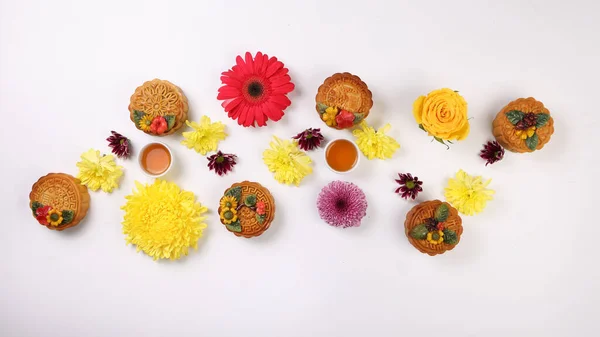 Colorful flower decorated moon cake Chinese mid autumn festival tea in small white teacup yellow violet chrysanthemum mum red daisy flower on white background