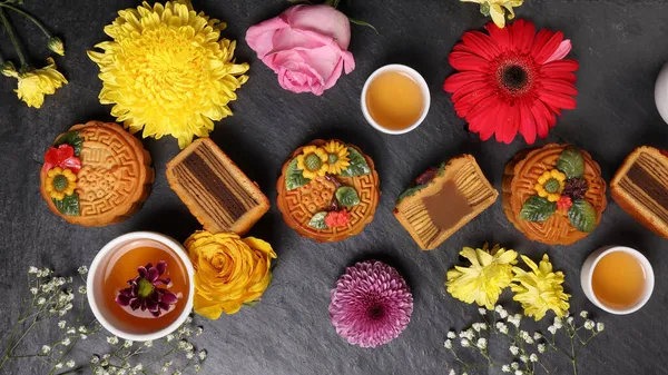 Colourful flower decorated mooncake Chinese mid autumn festival black slate stone background white teacup glass teapot daisy chrysanthemum mum rose baby breath flower red yellow pink purple violet