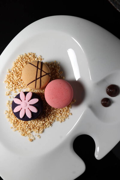 Assortment of mini decorated macaroon on bed of caramel chocolate sauce on white ceramic plate