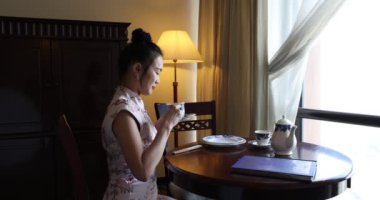 Asya kökenli, orta yaşlı, Cheongsam 'lı çekici bir kadın. Eski moda masa sandalyesinde oturuyor. Dolap lambası. 