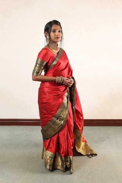 Indian woman wearing red orange traditional royal saree jewellery choker set necklace jhumka earring maang tikka waist chain stand pose look see smile mood expression at old rustic room background