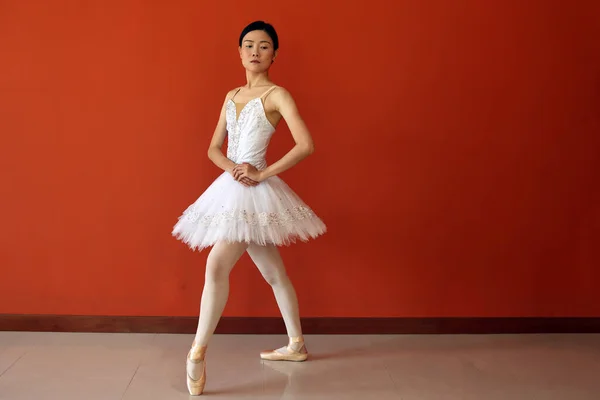 Beautiful Asian woman ballet dancer practice dance jump move wearing tutu at home red orange background wall