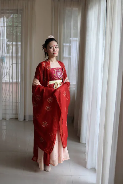 若い魅力的なアジアの女性は 屋内自然光を耳に伝統的な中国の赤い半布の長いスカートのドレスの衣装スカーフヘアピンを着て — ストック写真