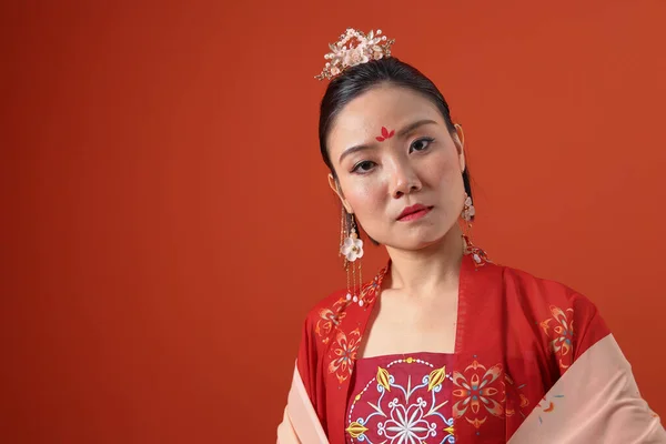 若い魅力的なアジアの女性を身に着けている伝統的な中国の赤い半布ロングスカートの衣装スカーフヘアピンピアス室内で読み取りマロンの背景壁 — ストック写真
